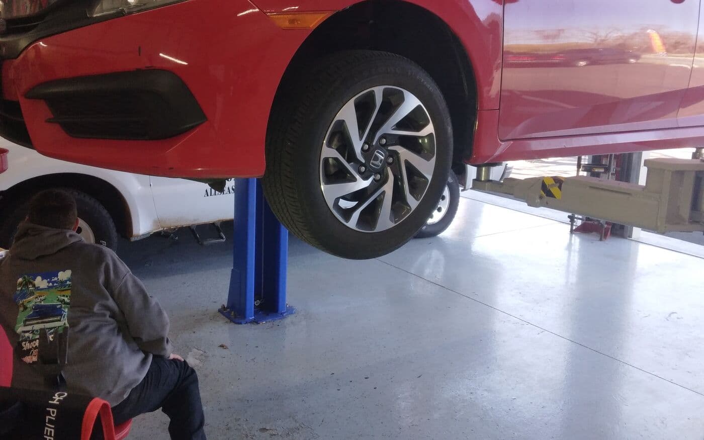 Red sedan raised on a lift while a technician works underneath