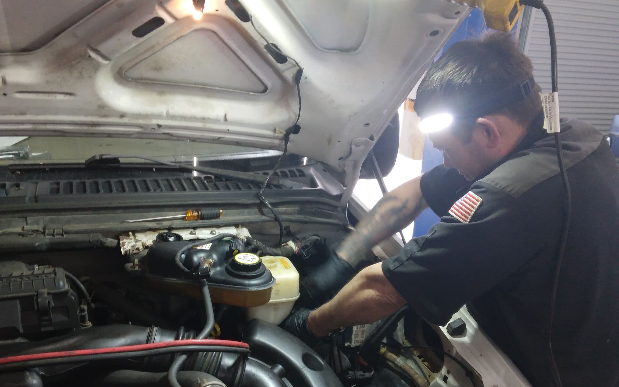 Shore Bro Auto technician with a headlamp working under the hood of a truck