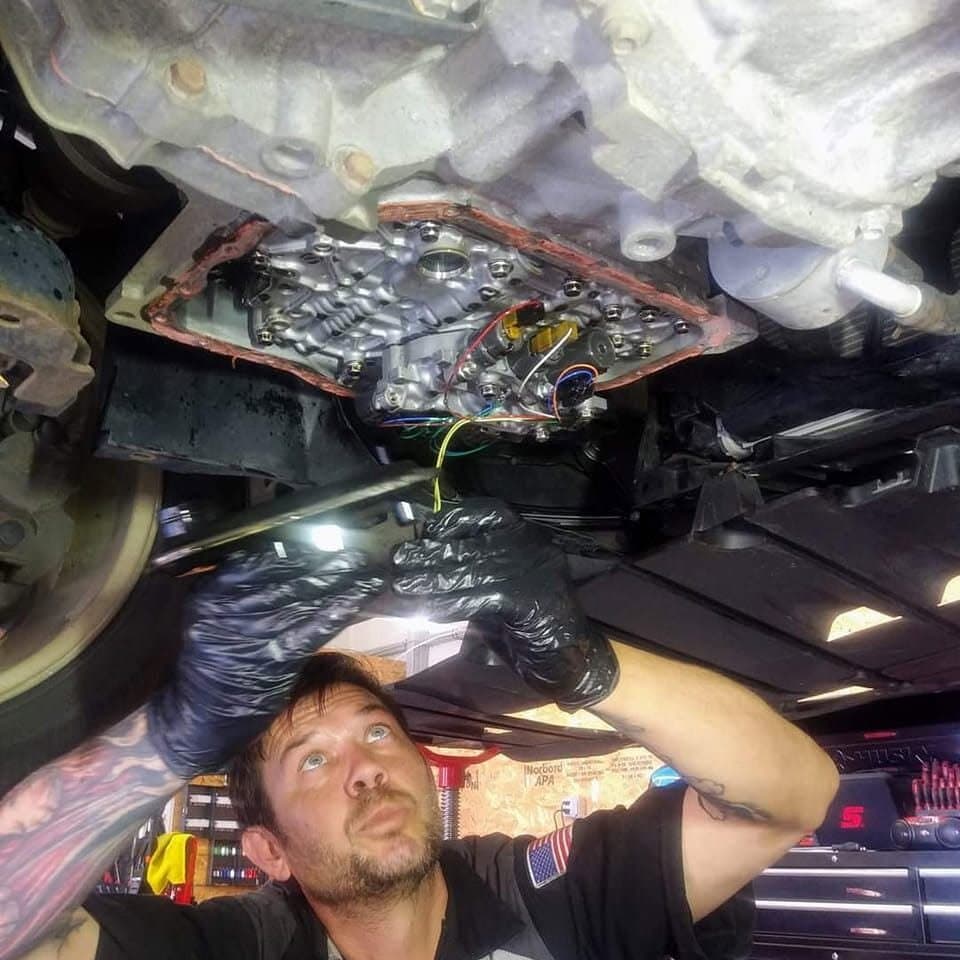 Shore Bro Auto technician working on a transmission valve body from under a car on the lift
